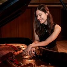 Ellen Sirower Ellen Sirower smiles and looks down into the inside of a grand piano. She wears a short-sleeved black shirt, brown pants, and a silver necklace. Her hands are crossed over the copper inside of the piano soundboard.